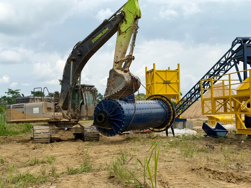 Broyeur à boulets élevé par une pelle hydraulique lors de son installation sur site.